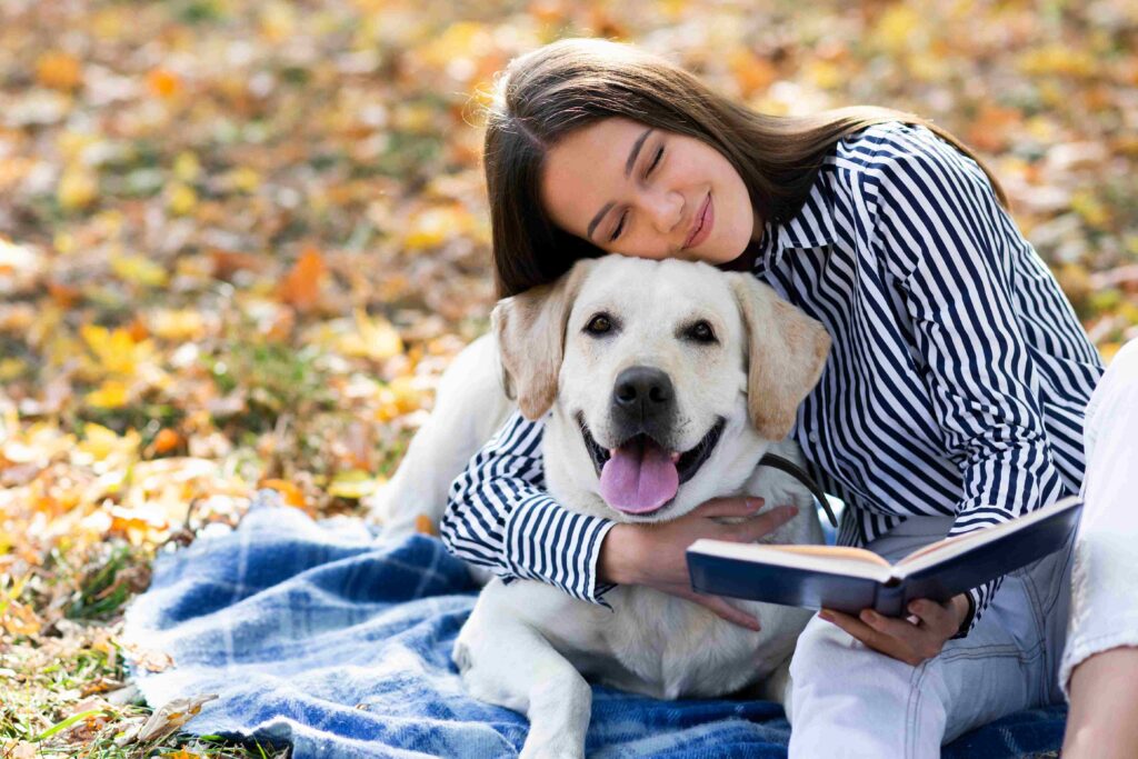 young woman outside reading a book with a senior dog